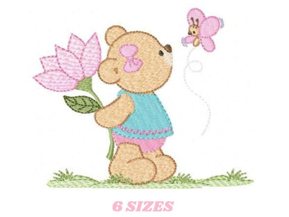 May include: Embroidered design of a brown teddy bear holding a pink flower and looking at a pink butterfly. The bear is wearing a blue dress with pink trim and pink shoes. The design is set against a green grassy background.